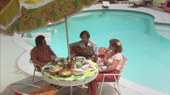 Movie still from “Straight Time” (1978), directed by Ulu Grosbard – A group of people sitting around a table with food on top of it; Wide shot, High angle