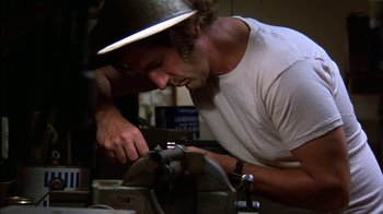 Movie still from “Straight Time” (1978), directed by Ulu Grosbard – A man wearing a hat is working on a machine; Close Up shot, Low angle