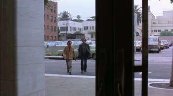 Movie still from “Straight Time” (1978), directed by Ulu Grosbard – Two people walking down the street in front of a building; Wide shot, Over the shoulder angle
