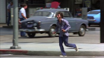 Movie still from “Straight Time” (1978), directed by Ulu Grosbard – A woman running down the street in front of a car; Wide shot, High angle