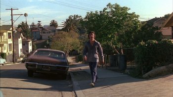Movie still from “Straight Time” (1978), directed by Ulu Grosbard – A man walking down a street next to an old car; Wide shot, Low angle