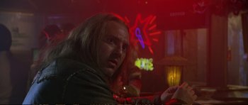 Movie still from “Strange Days” (1995), directed by Kathryn Bigelow – A man with long blonde hair is looking at the camera in front of a neon sign; Close Up shot, Low angle