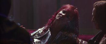 Movie still from “Strange Days” (1995), directed by Kathryn Bigelow – A woman with pink hair sitting on top of a couch; Close Up shot, Low angle