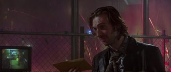 Movie still from “Strange Days” (1995), directed by Kathryn Bigelow – A man holding an envelope while standing in front of a fence; Close Up shot, Over the shoulder angle