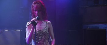 Movie still from “Strange Days” (1995), directed by Kathryn Bigelow – A woman is singing into a microphone in front of a crowd; Medium shot, Low angle