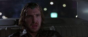 Movie still from “Strange Days” (1995), directed by Kathryn Bigelow – A man wearing a head piece sitting in the back of a car; Close Up shot, Low angle