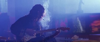 Movie still from “Strange Days” (1995), directed by Kathryn Bigelow – A person sitting on a stage with a guitar; Medium shot, Low angle