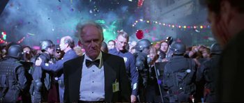 Movie still from “Strange Days” (1995), directed by Kathryn Bigelow – An older man in a tuxedo is in front of a group of people; Medium shot, Low angle