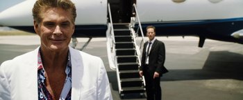 Movie still from “Stretch” (2014), directed by Joe Carnahan – A man in a suit and tie standing next to an airplane; Close Up shot, Over the shoulder angle