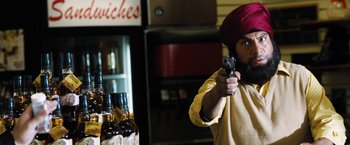 Movie still from “Stretch” (2014), directed by Joe Carnahan – A man in a turban is holding a gun in his hand; Medium shot, Over the shoulder angle