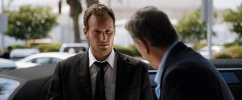 Movie still from “Stretch” (2014), directed by Joe Carnahan – A man in a suit and tie standing next to another man; Close Up shot, Over the shoulder angle