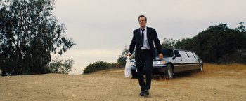 Movie still from “Stretch” (2014), directed by Joe Carnahan – A man in a suit and tie walking on a dirt road; Wide shot, Low angle
