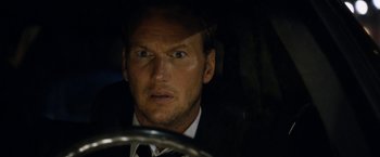 Movie still from “Stretch” (2014), directed by Joe Carnahan – A person wearing a suit driving a car; Close Up shot, Over the shoulder angle