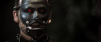 Movie still from “Stretch” (2014), directed by Joe Carnahan – A man wearing a leather mask with red eyes; Close Up shot, Low angle