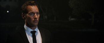 Movie still from “Stretch” (2014), directed by Joe Carnahan – A man wearing a suit and tie standing in the dark; Close Up shot, Over the shoulder angle