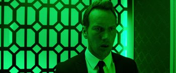Movie still from “Stretch” (2014), directed by Joe Carnahan – A man wearing a suit and tie in front of a green wall; Close Up shot, Low angle