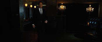 Movie still from “Stretch” (2014), directed by Joe Carnahan – A man in a suit and tie standing in a dark room; Medium shot, Low angle