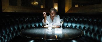 Movie still from “Stretch” (2014), directed by Joe Carnahan – A man sitting at a table with a plate of food and a glass of wine in front of him; Medium shot, Low angle