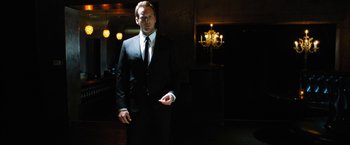Movie still from “Stretch” (2014), directed by Joe Carnahan – A man in a suit and tie in a dark room; Medium shot, Low angle