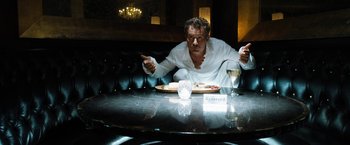 Movie still from “Stretch” (2014), directed by Joe Carnahan – A man sitting at a table with a plate of food in front of him; Medium shot, Low angle