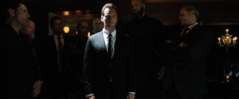 Movie still from “Stretch” (2014), directed by Joe Carnahan – A man in a suit and tie standing in front of other men; Medium shot, Low angle