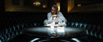 Movie still from “Stretch” (2014), directed by Joe Carnahan – A man sitting at a table with a plate of food in front of him; Medium shot, Low angle