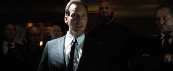 Movie still from “Stretch” (2014), directed by Joe Carnahan – A man wearing a suit and tie standing next to another man; Close Up shot, Low angle