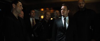 Movie still from “Stretch” (2014), directed by Joe Carnahan – A group of men standing next to each other in a room; Medium shot, Low angle