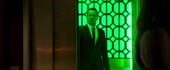 Movie still from “Stretch” (2014), directed by Joe Carnahan – A man in a suit and tie standing in front of a green wall; Medium shot, Low angle