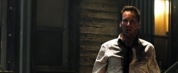 Movie still from “Stretch” (2014), directed by Joe Carnahan – A man wearing a tie standing in front of a brick wall; Close Up shot, Over the shoulder angle