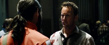 Movie still from “Stretch” (2014), directed by Joe Carnahan – A man with blood all over his face is talking to another man in an orange suit; Close Up shot, Over the shoulder angle