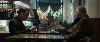 Movie still from “Suburra” (2015), directed by Stefano Sollima – A person sitting at a table with a glass of water; Medium shot, Over the shoulder angle