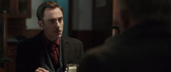 Movie still from “Suburra” (2015), directed by Stefano Sollima – A man sitting at a table with a drink in front of him; Close Up shot, Over the shoulder angle