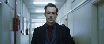 Movie still from “Suburra” (2015), directed by Stefano Sollima – A man in a suit and tie standing in a hallway; Close Up shot, Low angle