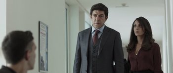 Movie still from “Suburra” (2015), directed by Stefano Sollima – A man in a suit and tie standing in front of a wall; Medium shot, Over the shoulder angle
