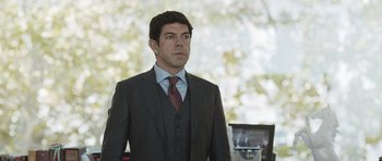 Movie still from “Suburra” (2015), directed by Stefano Sollima – A man in a suit and tie standing in front of a window; Medium shot, Over the shoulder angle