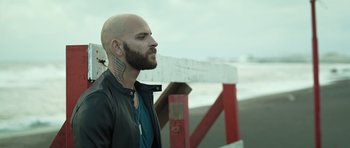 Movie still from “Suburra” (2015), directed by Stefano Sollima – A man with a beard and a tattoo on his face; Close Up shot, Over the shoulder angle