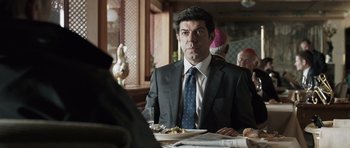 Movie still from “Suburra” (2015), directed by Stefano Sollima – A man sitting at a table with food in front of him; Medium shot, Over the shoulder angle