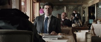 Movie still from “Suburra” (2015), directed by Stefano Sollima – A man sitting at a table in front of other people; Close Up shot, Over the shoulder angle