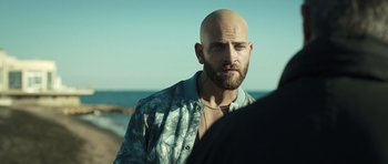 Movie still from “Suburra” (2015), directed by Stefano Sollima – A man with a bald head is standing on the beach; Close Up shot, Over the shoulder angle