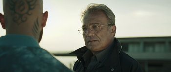 Movie still from “Suburra” (2015), directed by Stefano Sollima – An older man wearing glasses and a black jacket; Close Up shot, Low angle