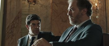 Movie still from “Suburra” (2015), directed by Stefano Sollima – Two men in business suits sitting at a table; Medium shot, Over the shoulder angle