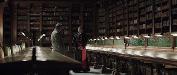 Movie still from “Suburra” (2015), directed by Stefano Sollima – Two men are standing in front of a long library table; Medium shot, High angle