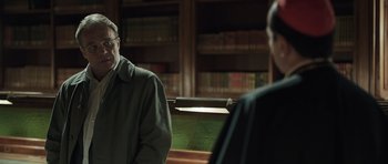 Movie still from “Suburra” (2015), directed by Stefano Sollima – A man in glasses and a green jacket in front of a book shelf; Medium shot, Over the shoulder angle