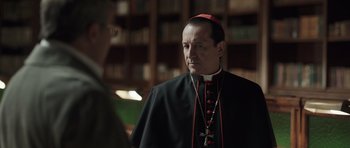 Movie still from “Suburra” (2015), directed by Stefano Sollima – A man wearing a black robe and a red hat; Close Up shot, Over the shoulder angle