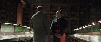 Movie still from “Suburra” (2015), directed by Stefano Sollima – Two men standing in front of a book shelf; Medium shot, Over the shoulder angle