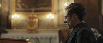 Movie still from “Suburra” (2015), directed by Stefano Sollima – A person in a room with lights in the background; Close Up shot, Over the shoulder angle