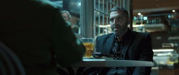 Movie still from “Suburra” (2015), directed by Stefano Sollima – A man sitting at a table in front of a glass of beer; Medium shot, Over the shoulder angle
