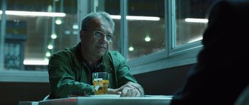 Movie still from “Suburra” (2015), directed by Stefano Sollima – An older man sitting at a table with a glass of beer; Close Up shot, Over the shoulder angle