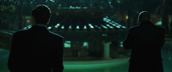 Movie still from “Suburra” (2015), directed by Stefano Sollima – A man in a suit standing in front of an illuminated ceiling; Medium shot, Low angle